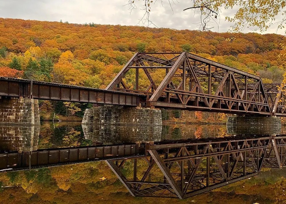 Iron train bridge over the Connecticut River with foliage trees behind it
