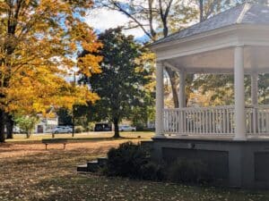 A white gazebo with a bench and large trees in the Brattleboro Commons.