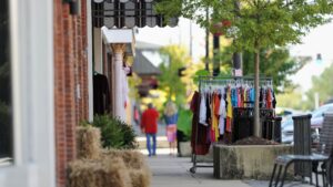 Clothing rack outside downtown Brattleboro shops with pedestrians walking along a tree-lined sidewalk.