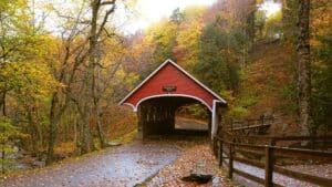 red covered bridge surrounded by colorful fall foliage and a quiet forest path in vermont