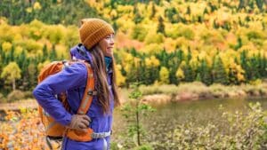 woman hiking in vermont wearing orange hat and backpack with colorful fall foliage in background