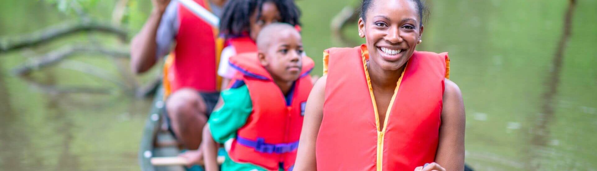 A family of four wearing life jackets while paddling a canoe in a river