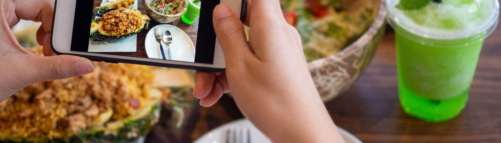 a person snapping a picture with their smartphone of the plated food on their table at a restaurant.