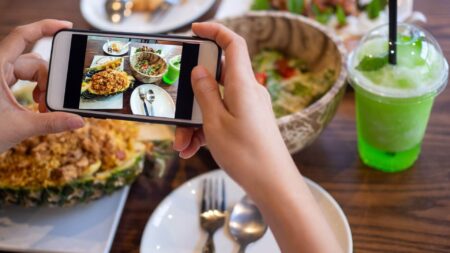 a person snapping a picture with their smartphone of the plated food on their table at a restaurant.