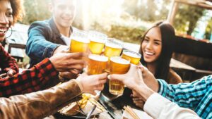 group of friends toasting beer pints with sandwiches and outdoor rustic seating