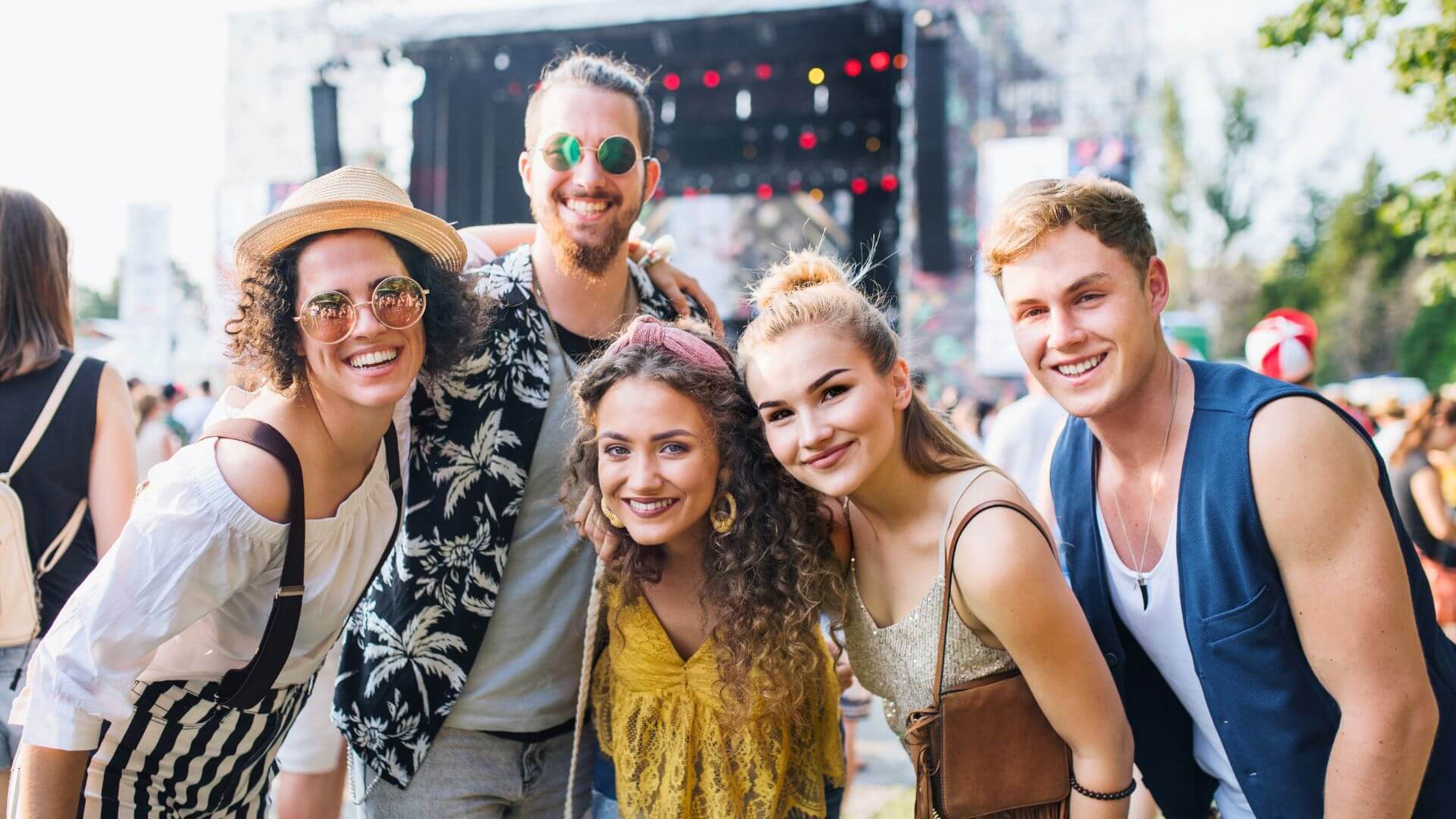 A cheerful group smiles together at an outdoor music festival filled with fun and excitement.